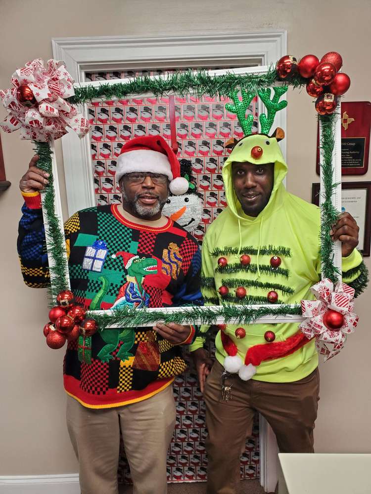 2 men from staff with holiday sweaters posing with frame