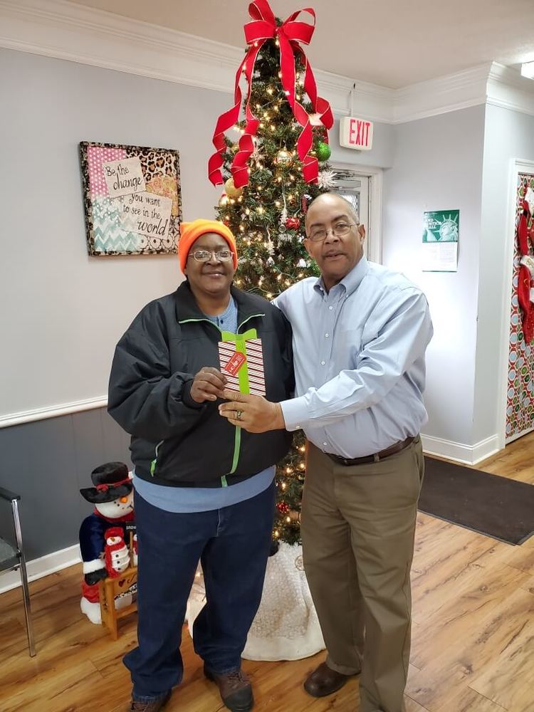 Connie Harris posing by Christmas tree receiving a gift