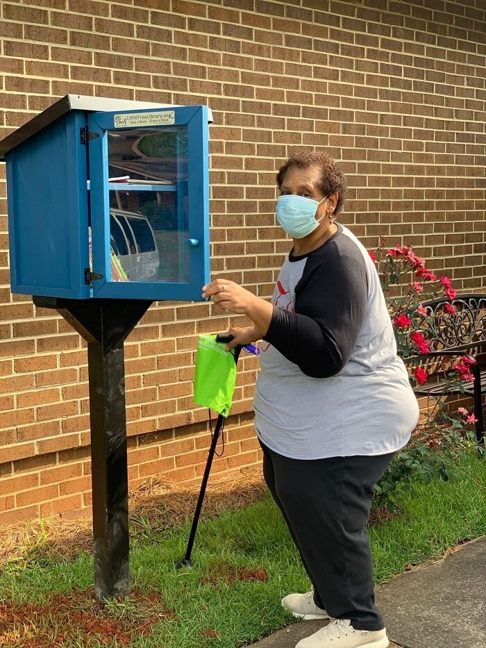 Woman wearing mask and holding cane at little library
